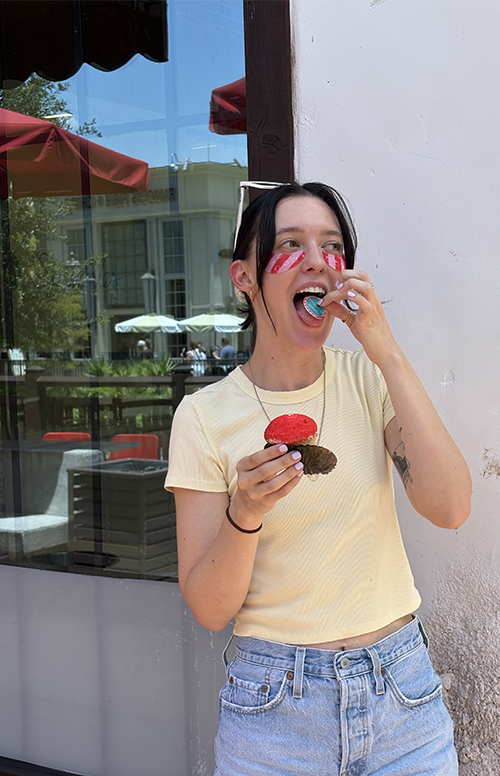 A picture of Aimee, the designer, eating a cupcake with her logo on it outside of a bakery in Disney Springs.